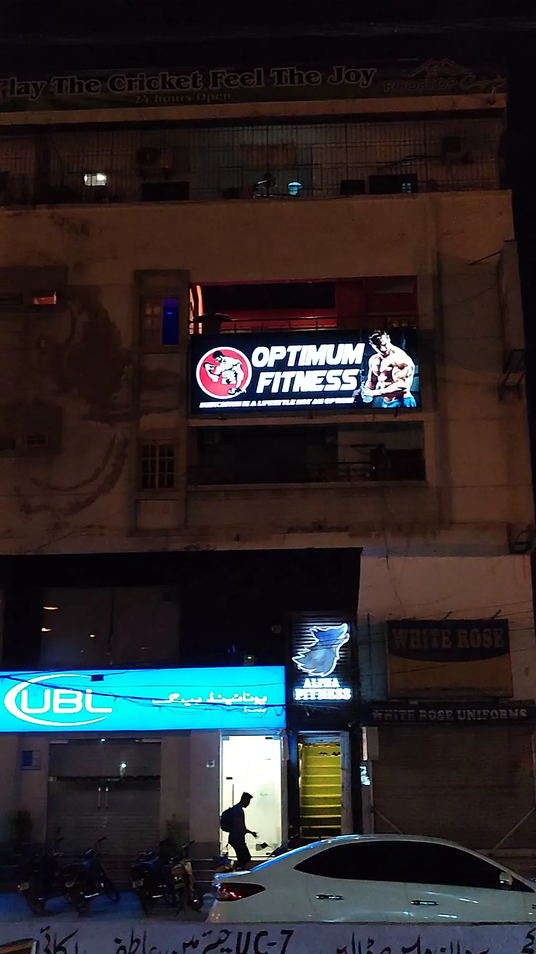 Optimum Fitness lit sign on Sir Syed Ahmed Road at night